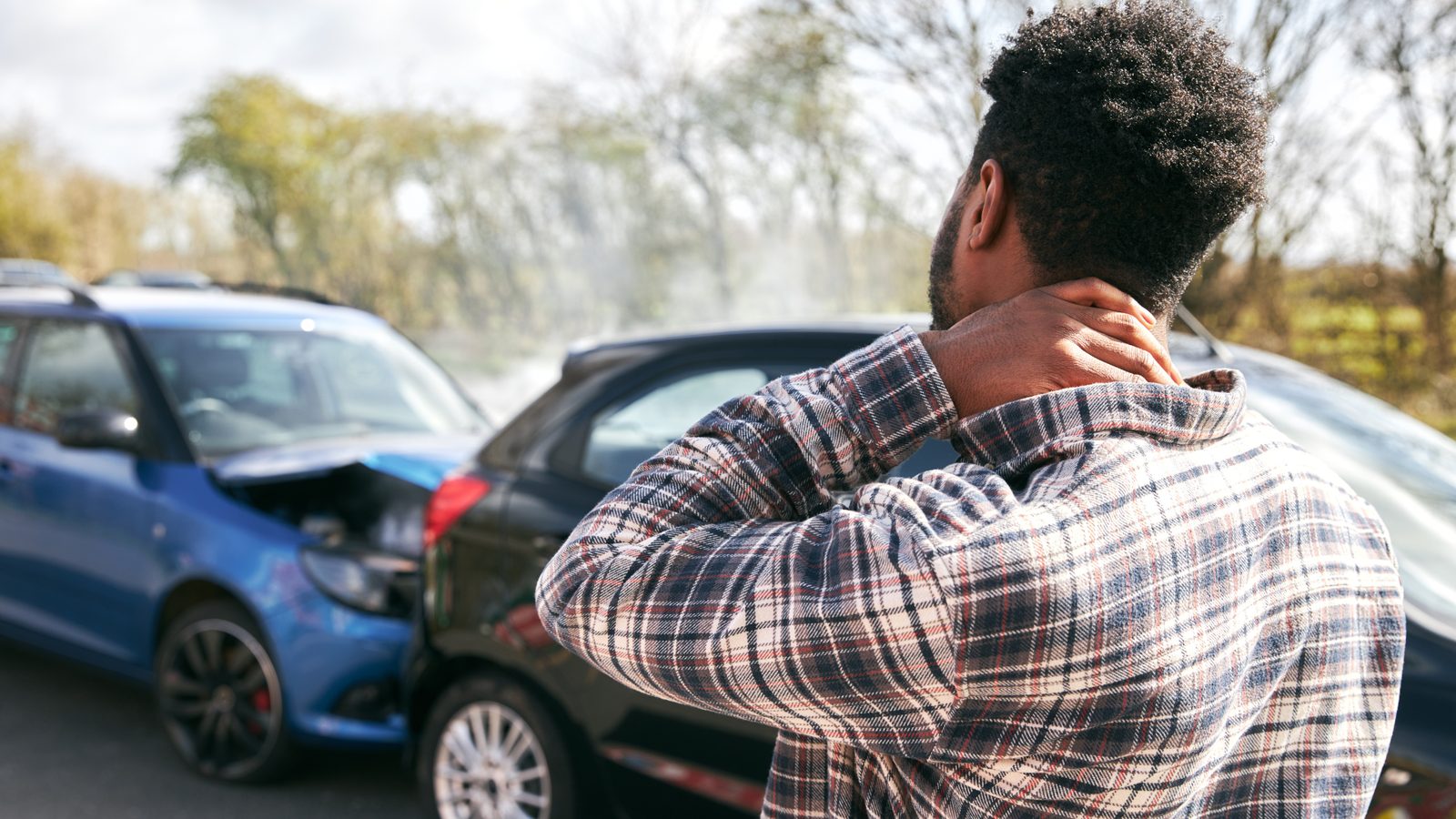 Man holding the back of his neck beside two damaged cars after a rear-end collision, a common sign of delayed whiplash symptoms