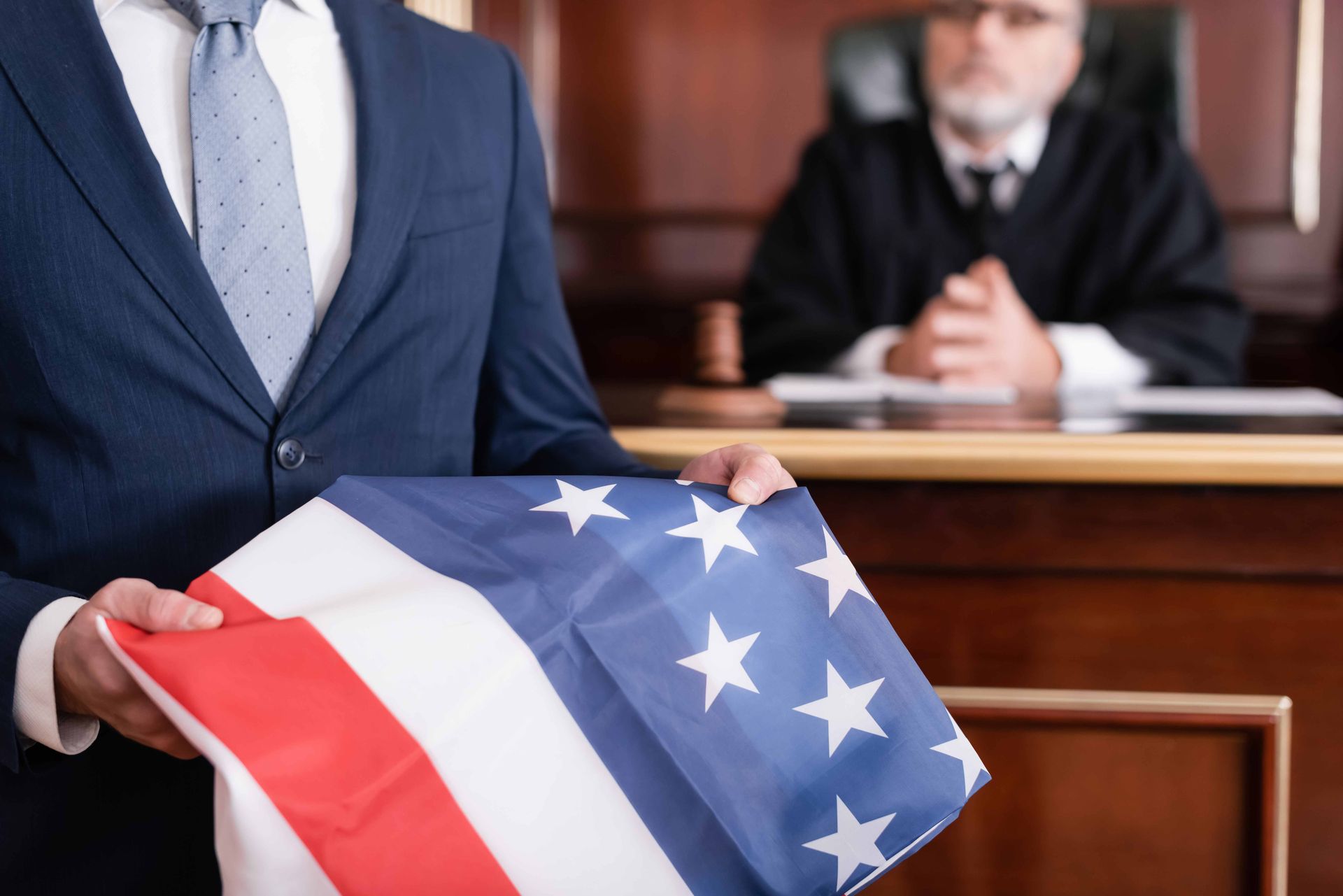 Attorney in a navy suit holding a folded American flag while standing before a judge in an Oregon courtroom
