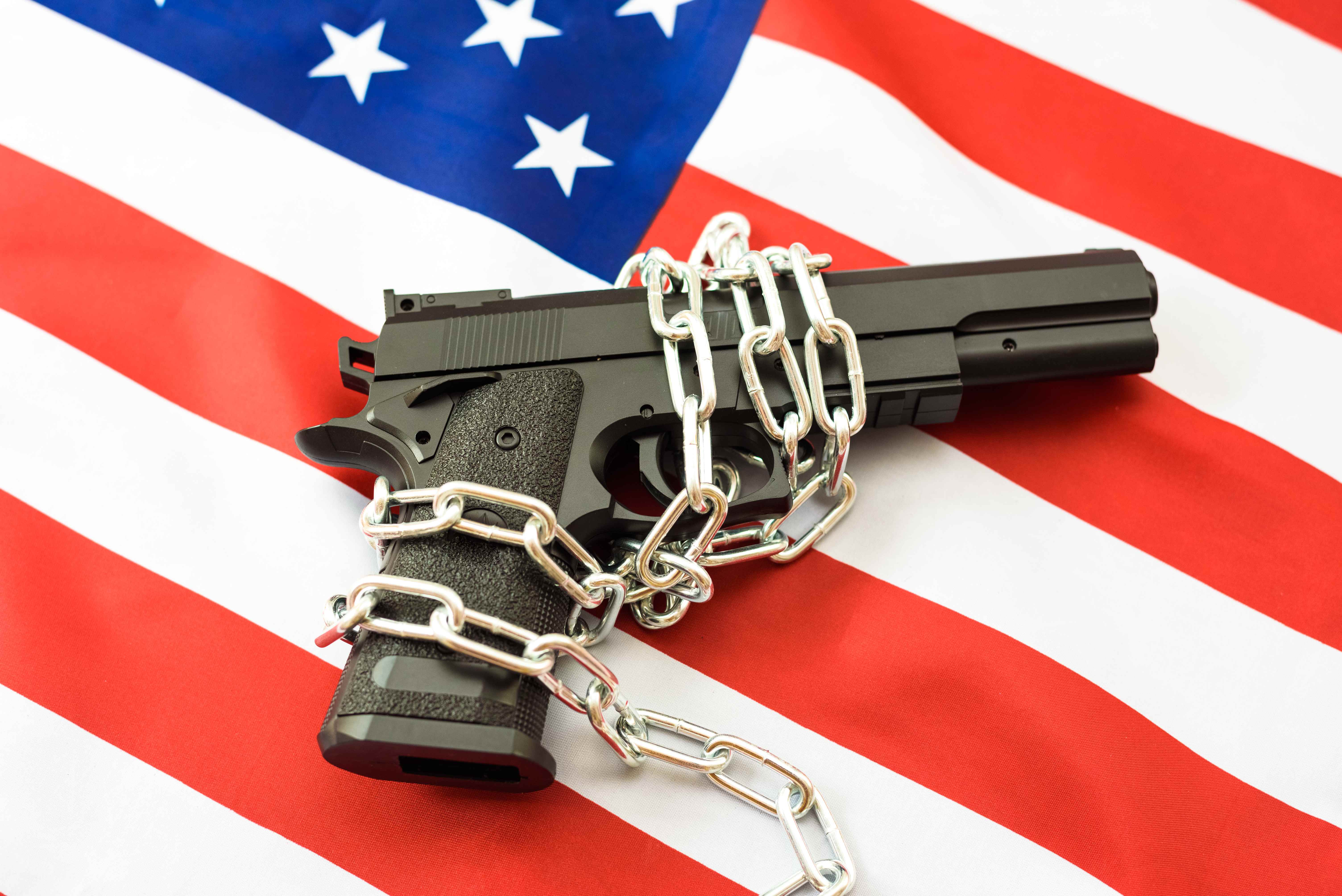 Handgun wrapped in heavy chains laid across an American flag — symbolizing constitutional rights restricted by a criminal record