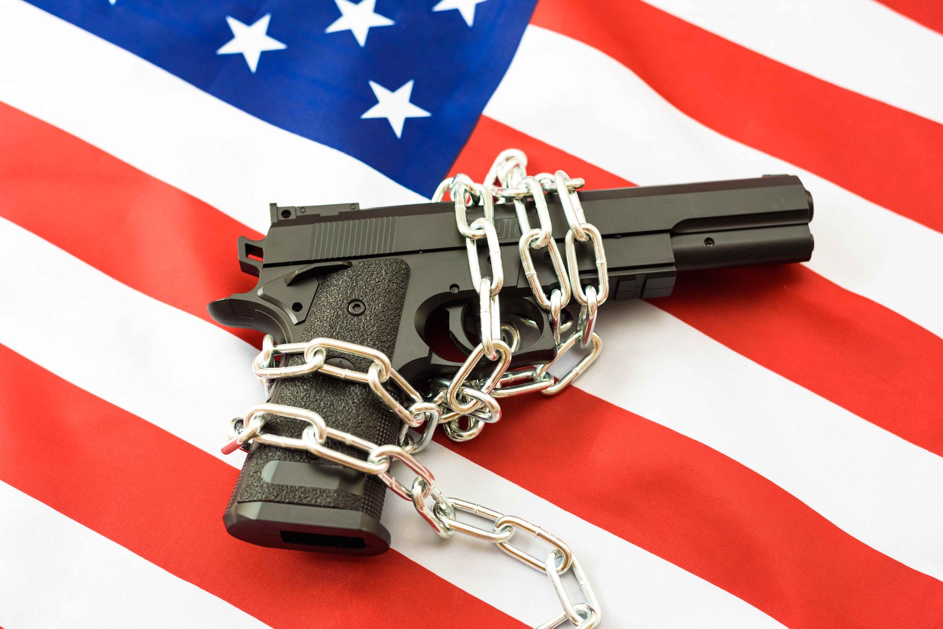 Handgun wrapped in heavy chains laid across an American flag — symbolizing constitutional rights restricted by a criminal record