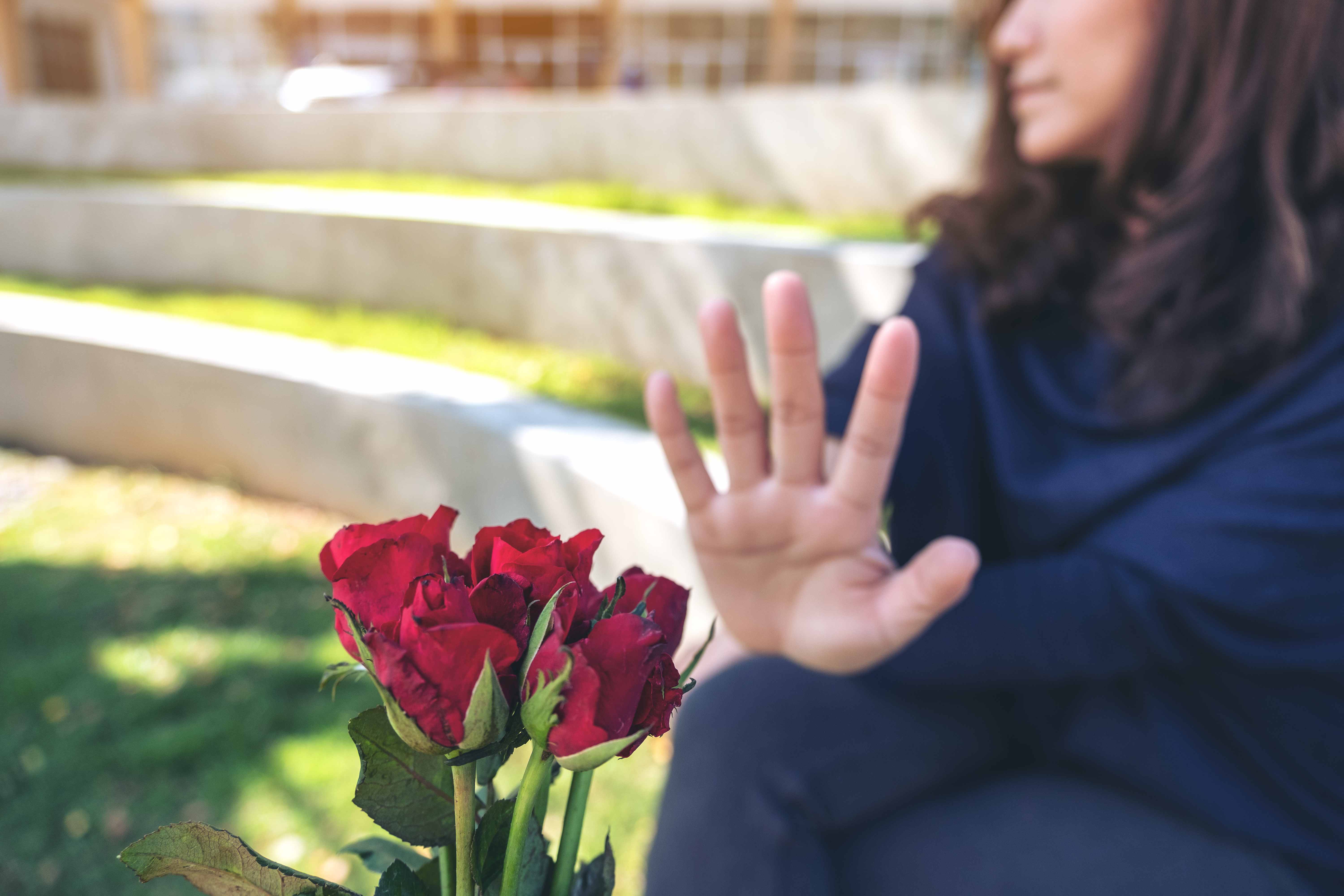 A grieving woman holding red roses extends her open hand in a refusal gesture — symbolizing rejecting an inadequate insurance settlement